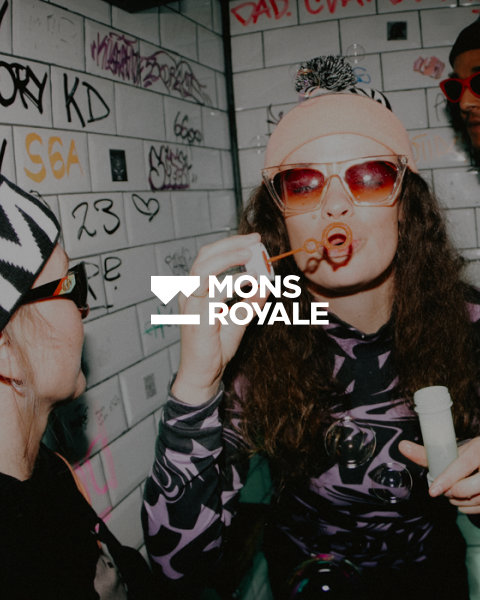 Due persone in una stanza decorata con graffiti. Una indossa occhiali da sole e un berretto e fa le bolle di sapone, mentre l'altra guarda con un cappello a fantasia e occhiali da sole. Al centro c'è il testo "MONS ROYALE".