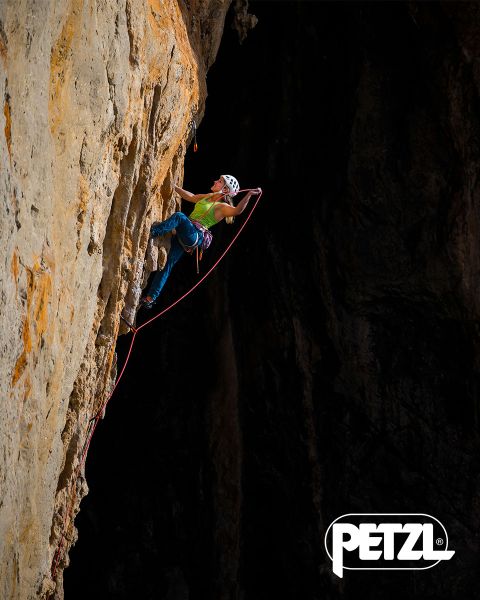 Un alpinista con giacca verde e casco scala una massiccia formazione di ghiaccio sospesa con piccozze. Rocce innevate circondano l'area. In alto campeggiano le parole "Vivi la differenza" e il logo Petzl.
