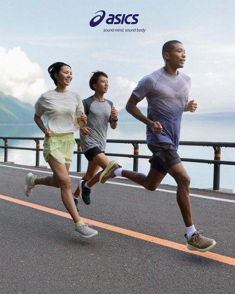 Tre persone corrono su una strada accanto a un grande specchio d'acqua con montagne sullo sfondo. Il cielo è parzialmente nuvoloso. Indossano abbigliamento sportivo e sembrano concentrati. Il logo ASICS e lo slogan sono in alto nell'immagine.