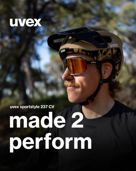Una persona con i baffi indossa occhiali UVEX Sportstyle e un casco all'aperto. Il testo recita: "UVEX sportstyle 237 CV made 2 perform". Sullo sfondo si vedono alberi e verde sfocato.