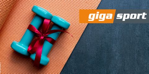 Zwei blaue Hanteln, mit einem roten Band zusammengebunden, liegen auf einer orangefarbenen Yogamatte. Oben rechts ist das „Giga Sport“-Logo zu sehen.