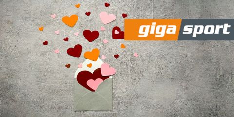 Ein geöffneter Umschlag mit roten, orangefarbenen und rosa Herzen auf strukturiertem grauem Hintergrund. Die Worte „Giga Sport“ sind in Orange und Grau dargestellt.