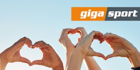 Vier Hände formen Herzen vor einem klaren blauen Himmel. Das „Giga Sport“-Logo befindet sich in der oberen rechten Ecke.
