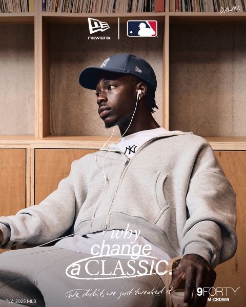 Un uomo in tuta grigia e cappellino dei New York Yankees è seduto rilassato ad ascoltare musica con le cuffie. Sono visibili i marchi New Era, MLB e 9FORTY M-CROWN, con il testo "Perché cambiare un classico?" che attraversa l'immagine.