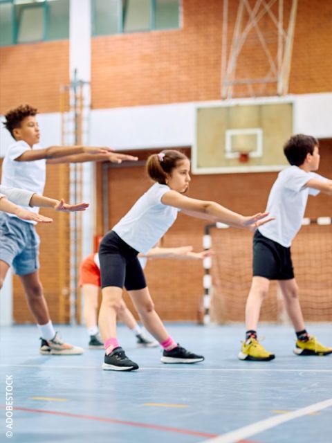 Primo piano di un bambino che indossa scarpe da ginnastica grigie con swoosh Nike rossi, in piedi su una superficie blu. Lo sfondo è sfocato con forme morbide e colorate.