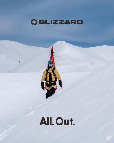 Due sciatori in abbigliamento invernale scendono una pista innevata. Lo sciatore a sinistra indossa un completo rosa, quello a destra uno beige. Entrambi indossano caschi e occhiali protettivi. Il logo Blizzard è visibile in alto a sinistra.