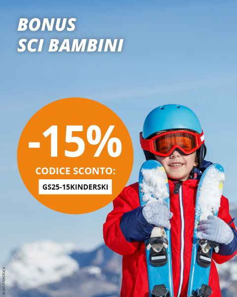 Un bambino sorridente con una giacca da sci rossa, un casco blu e occhiali da sci arancioni tiene gli sci su una montagna innevata. Il testo offre uno sconto del 15% per il bonus sci per bambini con il codice GS25-15KINDERSKI.