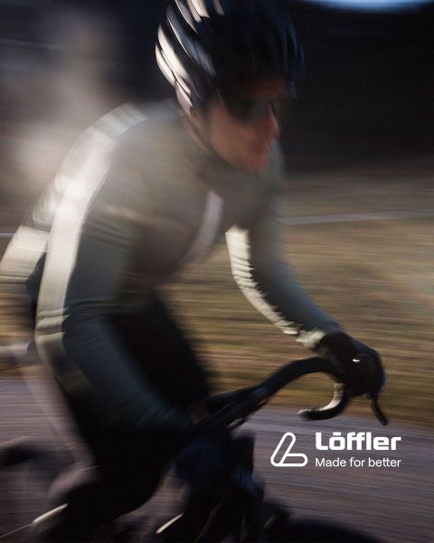 Due mountain biker percorrono un sentiero roccioso in mezzo a una vegetazione lussureggiante. Entrambi indossano caschi e occhiali da sole. Nell'angolo in basso a destra si legge la scritta "Löffler Made for better".