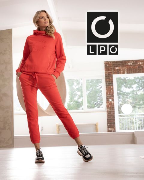 Un uomo in maglietta blu e pantaloni scuri esegue un esercizio con la battle rope in una palestra in stile industriale con due grandi finestre ad arco sullo sfondo. La luce entra e nell'angolo in alto a destra compaiono le lettere "LPO".