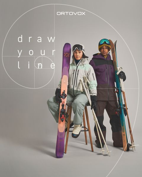 Tre persone con abbigliamento da outdoor sono sedute su un terreno roccioso in una regione montuosa, sorridendo e chiacchierando. Il sole tramonta dietro le cime. Uno zaino e un thermos sono nelle vicinanze. Il logo di Ortovox si trova in alto a destra.