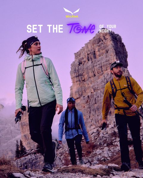 Una persona in giacca bianca e occhiali da sole si arrampica su un terreno roccioso. L'effetto di sfocatura del movimento enfatizza la velocità e il movimento. In alto c'è il testo "MXT Forward A Fast Story", a destra il logo Salewa.