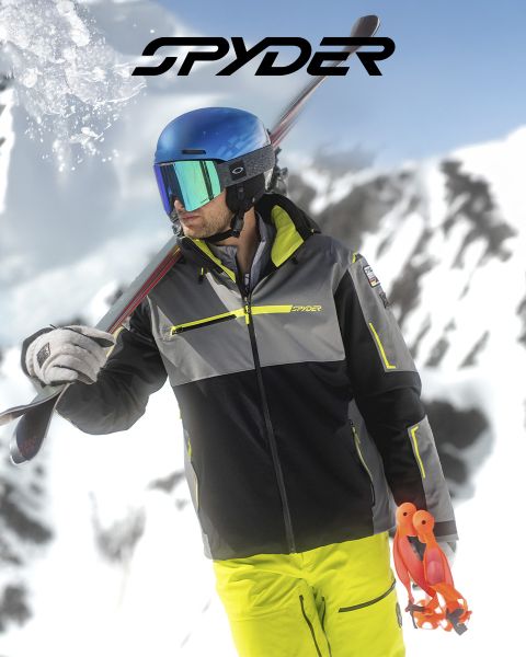 Uno sciatore in tenuta nera e gialla scende un pendio innevato, con un paesaggio innevato sullo sfondo. In alto c'è il testo: "SPYDER PER SCIATORI DAL 1978". Nell'angolo in basso a destra c'è un piccolo logo bianco a forma di ragno.