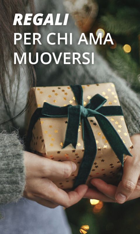 Primo piano di mani che tengono un regalo avvolto in carta marrone con stelle dorate e un nastro verde scuro. Il testo sopra recita: "Regali per chi ama muoversi".