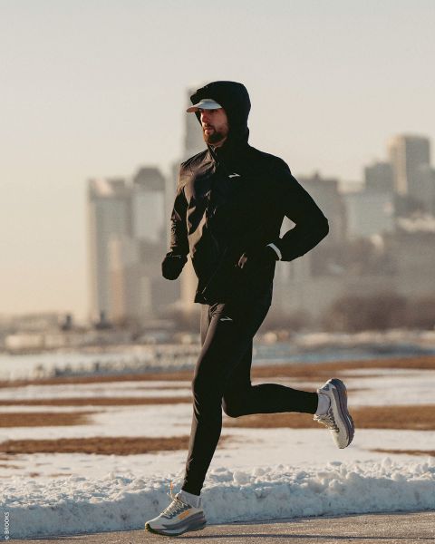 Una persona in abbigliamento sportivo fa jogging su un sentiero innevato in una giornata limpida, con lo skyline della città sullo sfondo.