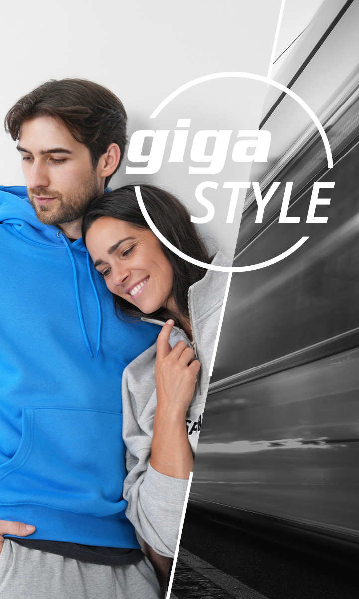 Un uomo con una felpa blu con cappuccio e una donna con una felpa grigia con cappuccio sorridono e si appoggiano l'uno all'altra. L'immagine è divisa diagonalmente, con il lato destro che mostra un treno in movimento sfocato e le parole "giga STYLE" sovrapposte.