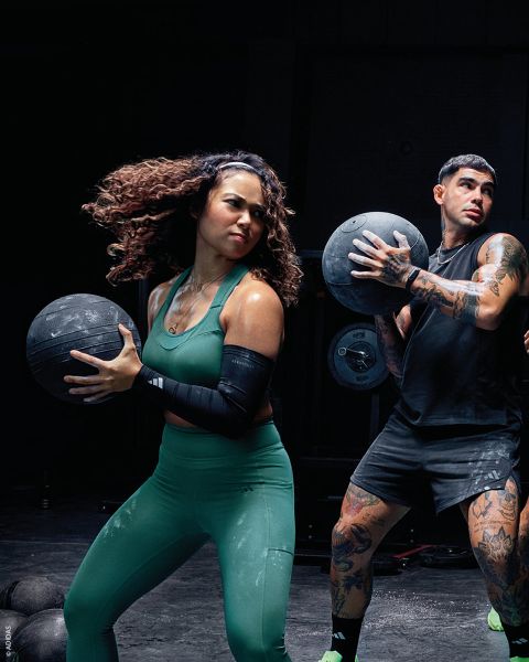 Due persone in abbigliamento sportivo tengono dei medicine ball mentre si allenano in una palestra. Entrambi sembrano concentrati e attivi.