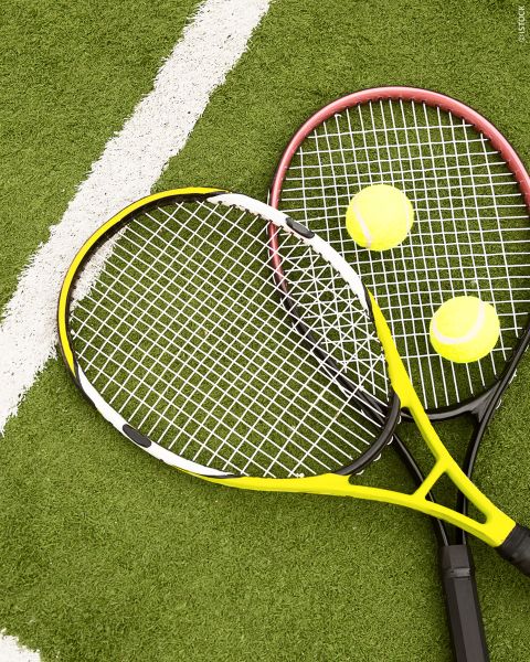 Due racchette da tennis e due palline da tennis giacciono su un campo verde con una linea bianca sullo sfondo.