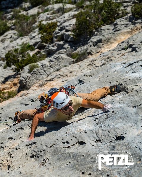 Un alpinista con giacca verde e casco scala una massiccia formazione di ghiaccio sospesa con piccozze. Rocce innevate circondano l'area. In alto campeggiano le parole "Vivi la differenza" e il logo Petzl.