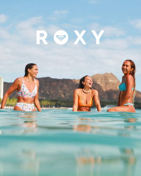 Tre donne nuotano sott'acqua in costume da bagno in acque limpide e blu. Una indossa una maglia a maniche lunghe, le altre dei bikini. L'immagine è sovrapposta al logo bianco "Roxy".