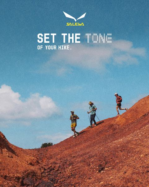 Una persona in giacca bianca e occhiali da sole si arrampica su un terreno roccioso. L'effetto di sfocatura del movimento enfatizza la velocità e il movimento. In alto c'è il testo "MXT Forward A Fast Story", a destra il logo Salewa.