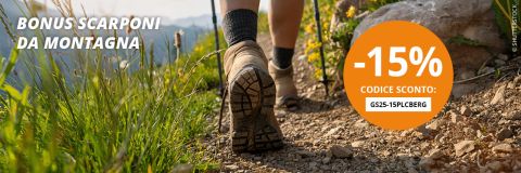 Una donna con uno zaino sta camminando su un sentiero di montagna roccioso, con cime innevate e nuvole sullo sfondo. Un cerchio arancione offre uno sconto del -15% con il codice GS25-15PLCIBERG. Il testo recita "Bonus Scarponi".