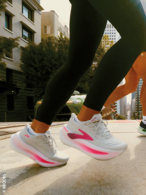 Due persone che corrono su una strada in città, con particolare attenzione alle loro gambe e alle scarpe da corsa bianche con accenti rosa.