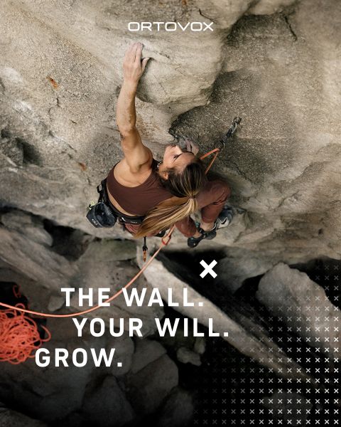 Tre persone con abbigliamento da outdoor sono sedute su un terreno roccioso in una regione montuosa, sorridendo e chiacchierando. Il sole tramonta dietro le cime. Uno zaino e un thermos sono nelle vicinanze. Il logo di Ortovox si trova in alto a destra.