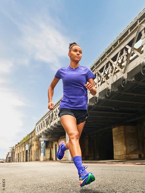 Una donna in abbigliamento sportivo corre all'aperto in una strada cittadina sotto un grande ponte di metallo in una giornata limpida.
