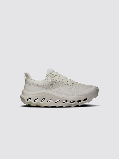 Una sneaker grigia con dettagli neri, suola bianca e un caratteristico logo "V" nero sul lato. La parola "SNEAKER" è scritta in grassetto bianco in alto a sinistra su uno sfondo grigio chiaro.