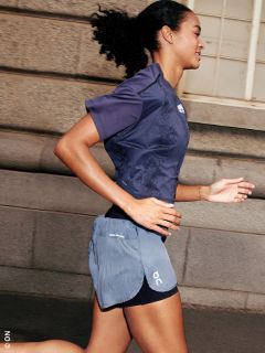 Donna fa jogging all'aperto in abbigliamento sportivo, sorride e corre davanti a un edificio in pietra con finestre.