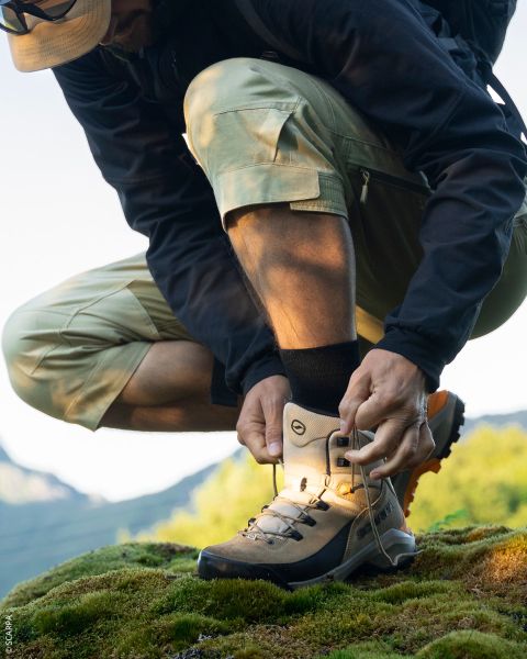 Primo piano di due escursionisti in piedi su un terreno roccioso, che guardano le loro scarpe da trail running La Sportiva sotto un cielo azzurro limpido.