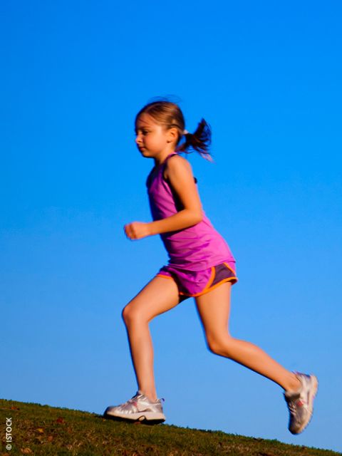 Giovane ragazza in un completo sportivo rosa che corre all'aperto su una collina con un cielo azzurro limpido sullo sfondo.