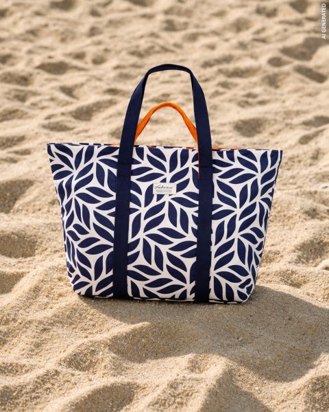 Una borsa tote blu navy e bianca con motivo a foglie e fodera interna arancione è appoggiata sulla spiaggia sabbiosa.