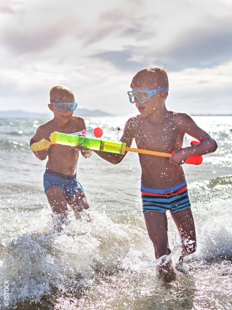 Due ragazzi con occhialini da nuoto giocano con una pistola ad acqua in mare e sguazzano tra le onde sotto un cielo luminoso e soleggiato.