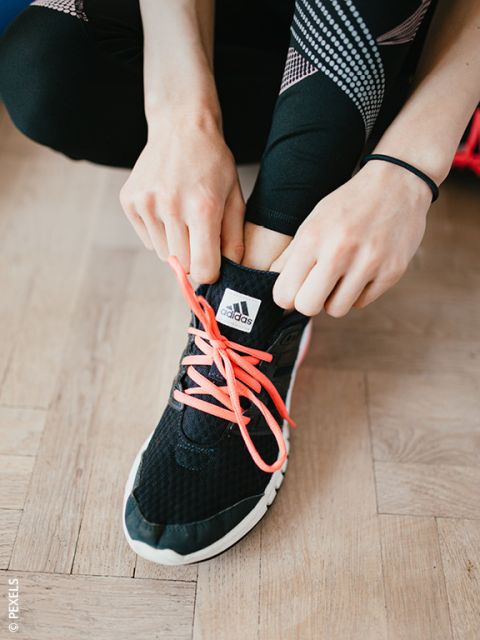 Una persona che allaccia lacci rosa shocking su una sneaker Adidas nera, indossando leggings neri con motivi bianchi e rosa.