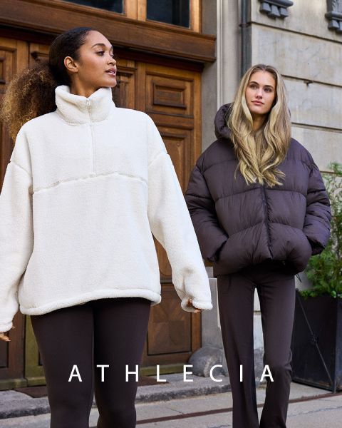 Due donne in abbigliamento sportivo Athlecia blu posano su un terreno roccioso. Una indossa una felpa e pantaloncini, l'altra un top corto bianco e pantaloni blu. Sopra di loro si vede il marchio "Athlecia".