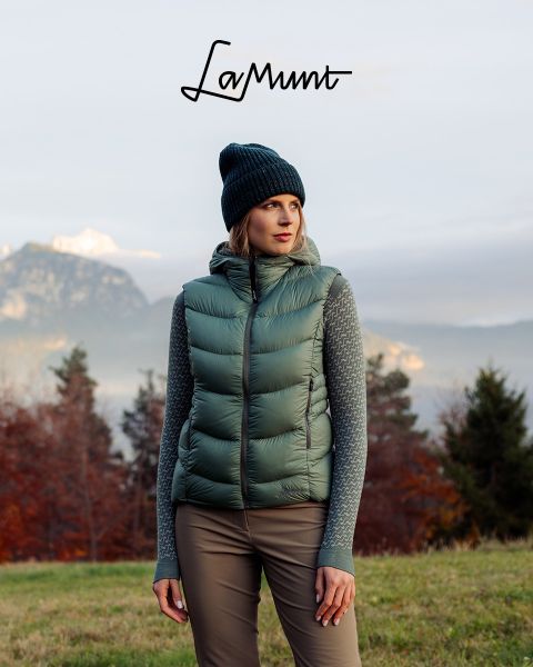 Tre persone in abbigliamento invernale sciano in un paesaggio montano innevato sotto un cielo limpido. Il testo recita: "LaMunt MOUNTAIN ME-TIME". Sullo sfondo si vedono cime innevate.
