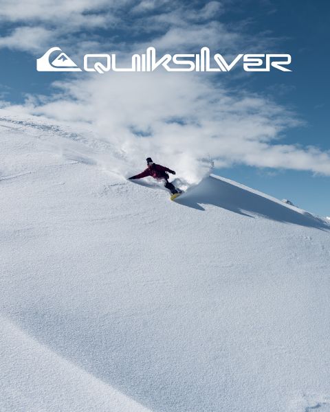 Un surfista cavalca una grande onda turchese, incarnando equilibrio e abilità. Indossa pantaloncini da bagno scuri e l'onda si increspa sopra di lui. Sopra di lui si vede il logo Quiksilver.
