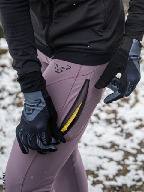 Due persone che corrono di notte in abbigliamento sportivo, con gocce di pioggia visibili nell'aria e marciapiede bagnato sotto di loro. Entrambi i corridori indossano giacche e scarpe da corsa e corrono velocemente davanti a un cancello di metallo.