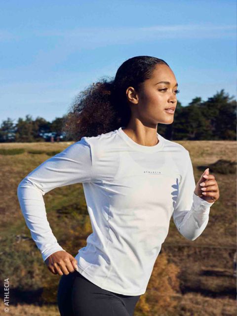 Quattro persone in abbigliamento da corsa invernale fanno jogging insieme su un sentiero innevato sotto un ponte di cemento, sorridendo e godendosi l'attività all'aperto.