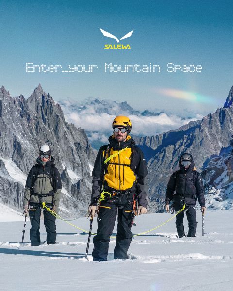 Una persona in giacca bianca e occhiali da sole si arrampica su un terreno roccioso. L'effetto di sfocatura del movimento enfatizza la velocità e il movimento. In alto c'è il testo "MXT Forward A Fast Story", a destra il logo Salewa.