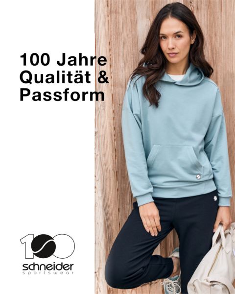 Una persona con capelli alle spalle, giacca casual e maglietta è in piedi davanti a uno sfondo neutro. Nella parte superiore dell'immagine si legge la scritta "Schneider Sportswear".