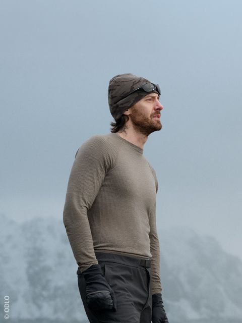 Un uomo e una donna in abbigliamento invernale casual sono seduti all'aperto su un muro di pietra, sorridono e chiacchierano. Un paio di sci sono appoggiati al muro e sullo sfondo si vedono montagne innevate.