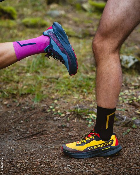 Due gambe con scarpe da trail running e calzini sportivi, in piedi su una strada sterrata.